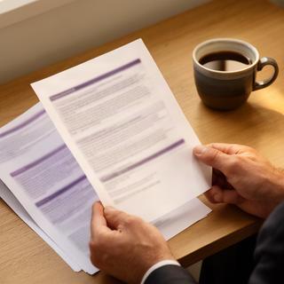 Persona leyendo condiciones legales impresas con una taza sobre el escritorio