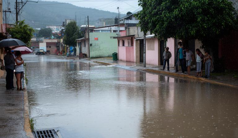 Calles de Cholula después de la lluvia, con vecinos observando una zona de agua acumulada